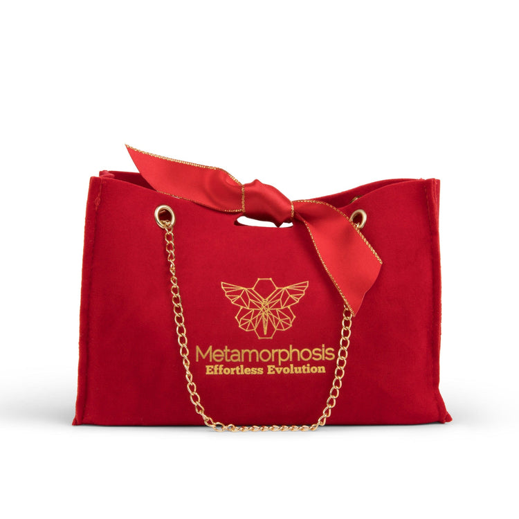 A red felt Metamorphosis gift bag with gold chains, a red ribbon bow, and the brand's gold butterfly logo with the text Effortless Evolution.