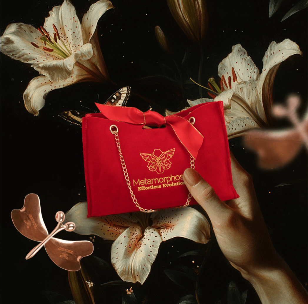 Metamorphosis luxurious red velvet gift bag with a gold chain, logo, and ribbon, featuring white lilies and a copper butterfly beauty tool