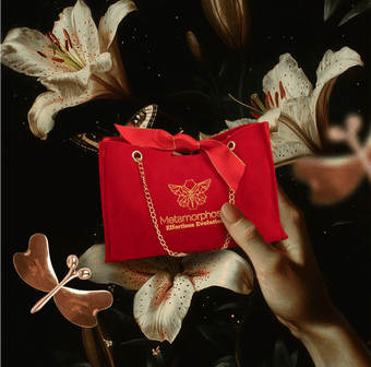 Metamorphosis luxurious red velvet gift bag with a gold chain, logo, and ribbon, featuring white lilies and a copper butterfly beauty tool