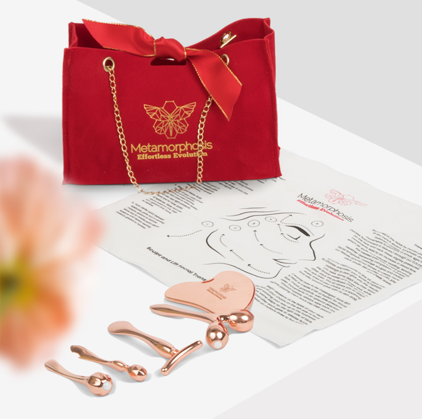 Metamorphosis luxurious red velvet gift bag with a gold chain, logo, and ribbon, featuring white lilies and a copper butterfly beauty tool