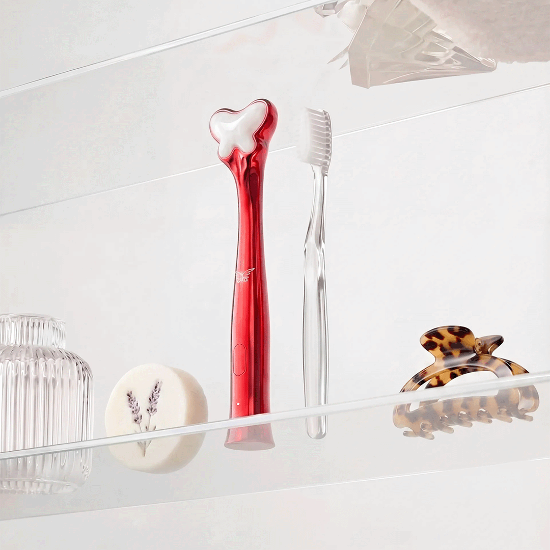 Metamorphosis Red electric toothbrush and clear manual toothbrush on a bathroom shelf with a tortoiseshell hair clip.