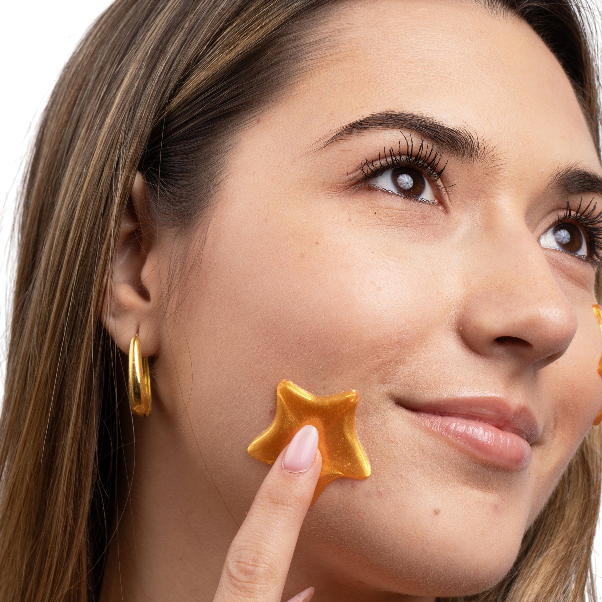 Metamorphosis  star-shaped hydrogel patch to her cheek, demonstrating the application of a skincare product for hydration or acne treatment