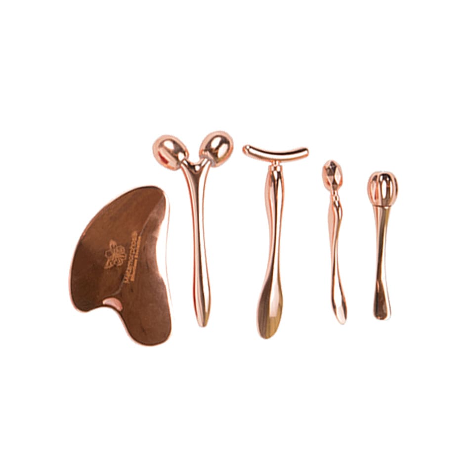 Five rose gold-toned Metamorphosis facial massage tools, including a Gua Sha scraper and various rollers, designed for facial sculpting, lifting, and anti-aging skincare routines.